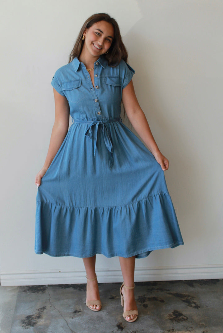 Woman wearing a blue dress standing against a white wall.