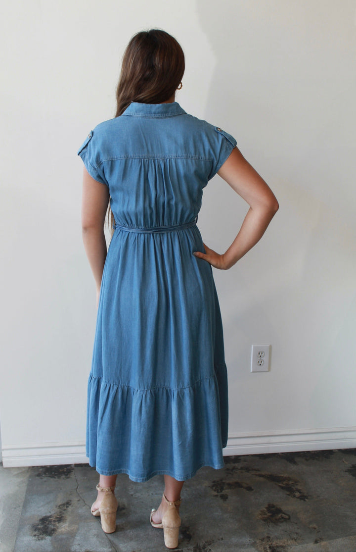 Woman wearing a blue dress standing in a room with a white wall and floor.
