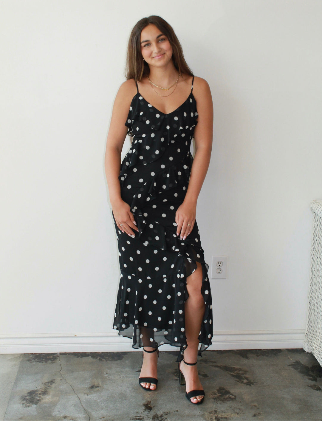 Woman wearing a black dress with white polka dots against a white wall.