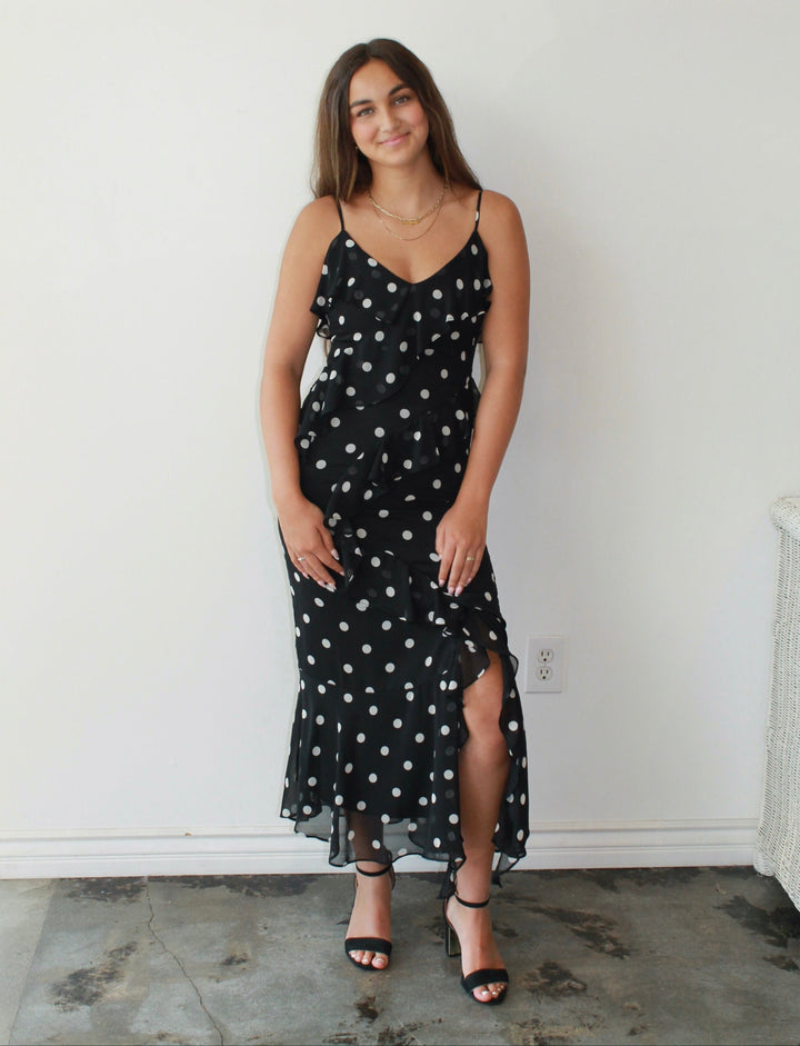 Woman wearing a black dress with white polka dots against a white wall.