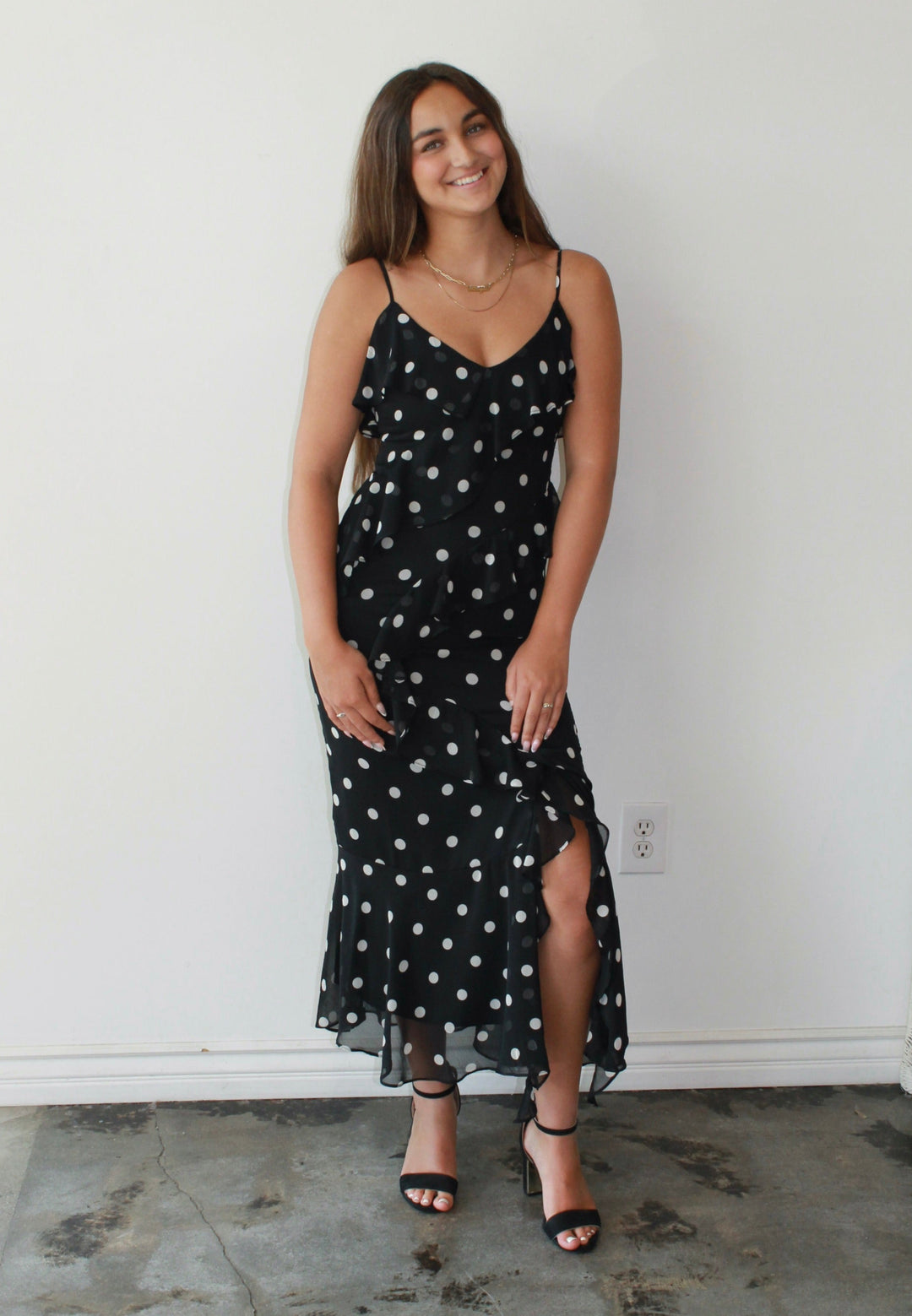 Woman wearing a black dress with white polka dots standing against a white wall.
