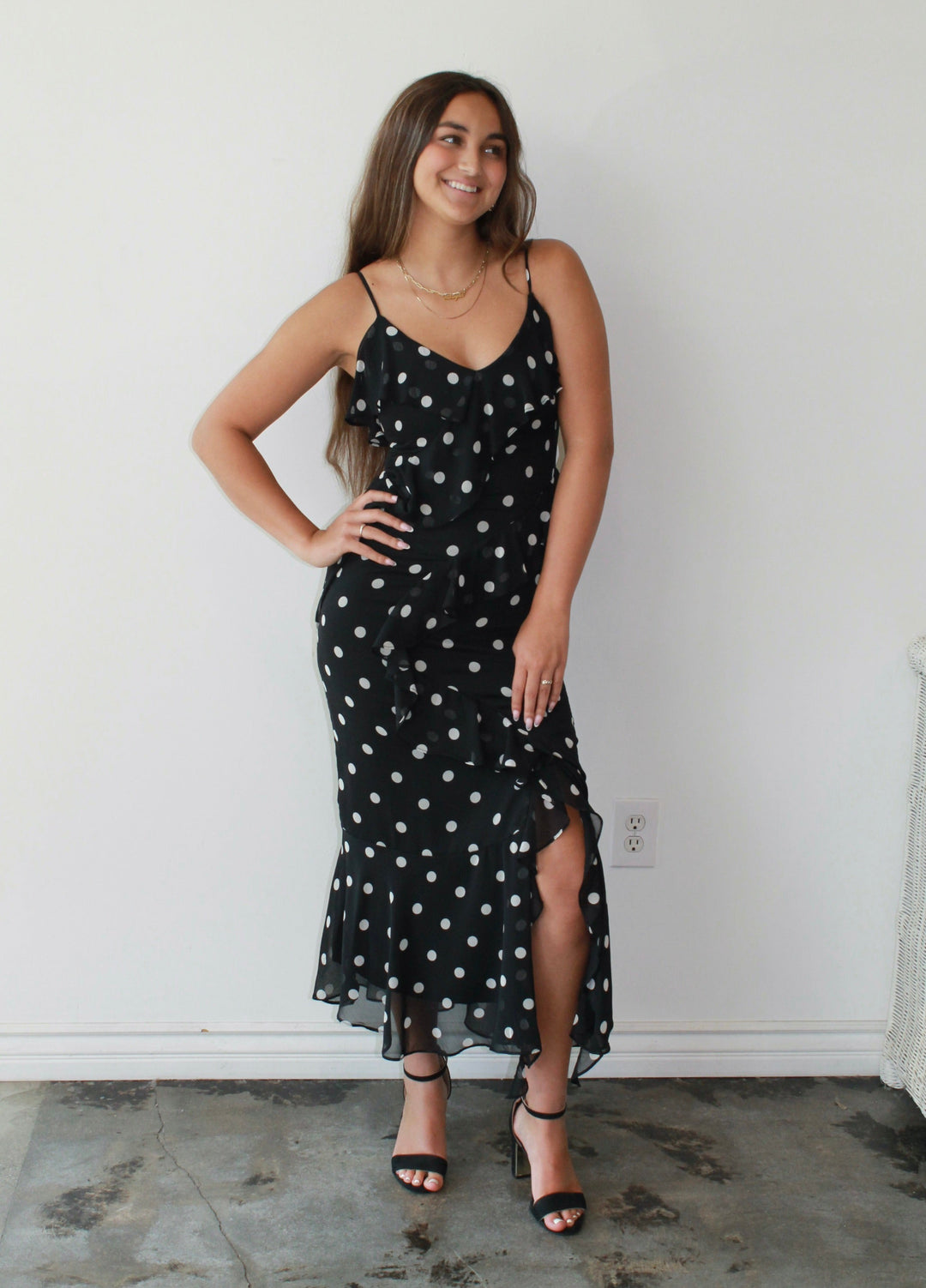 Woman wearing a black dress with white polka dots against a white wall.