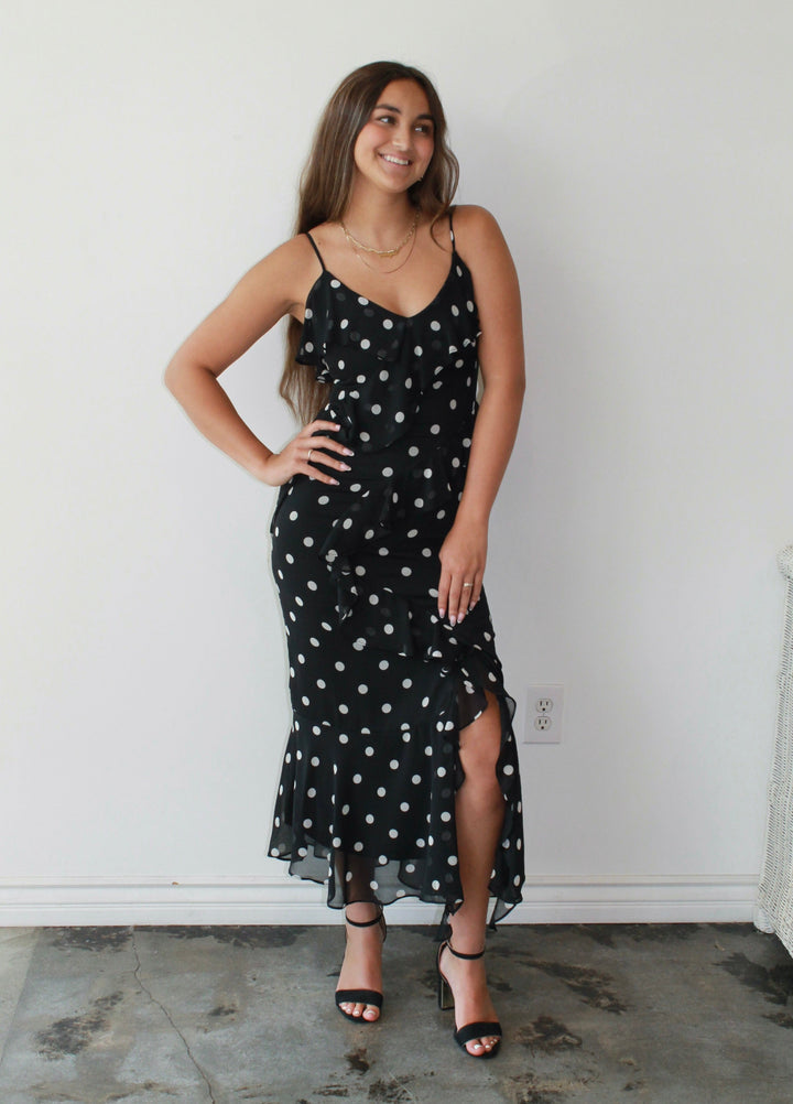 Woman wearing a black dress with white polka dots against a white wall.
