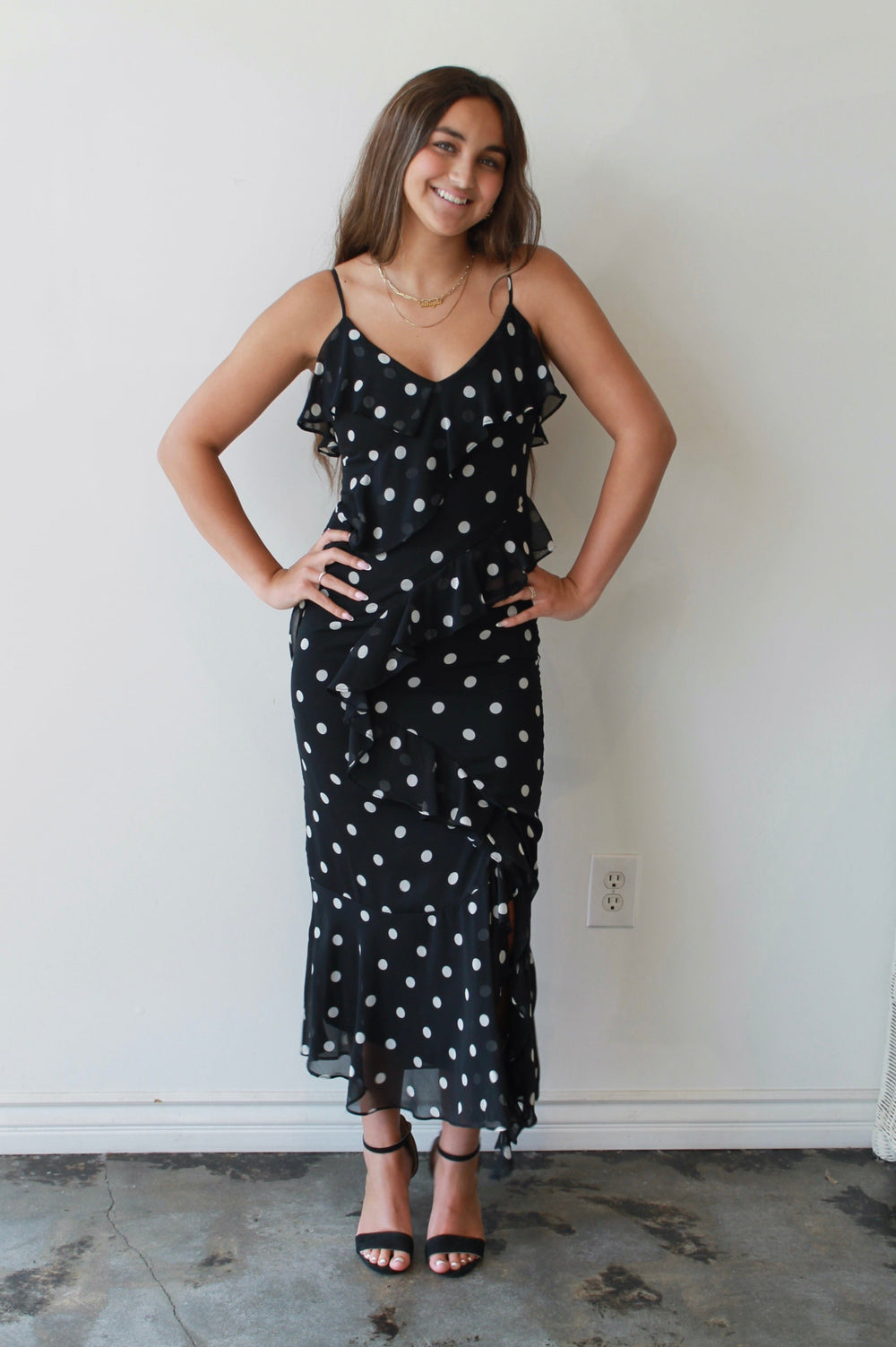 Woman wearing a black dress with white polka dots against a plain wall.