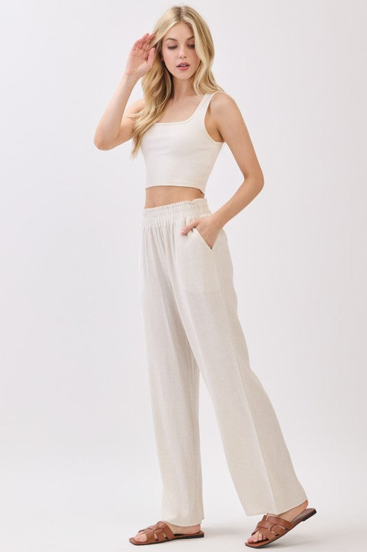 Beige linen wide leg pants styled with sleeveless crop top and sandals on white background